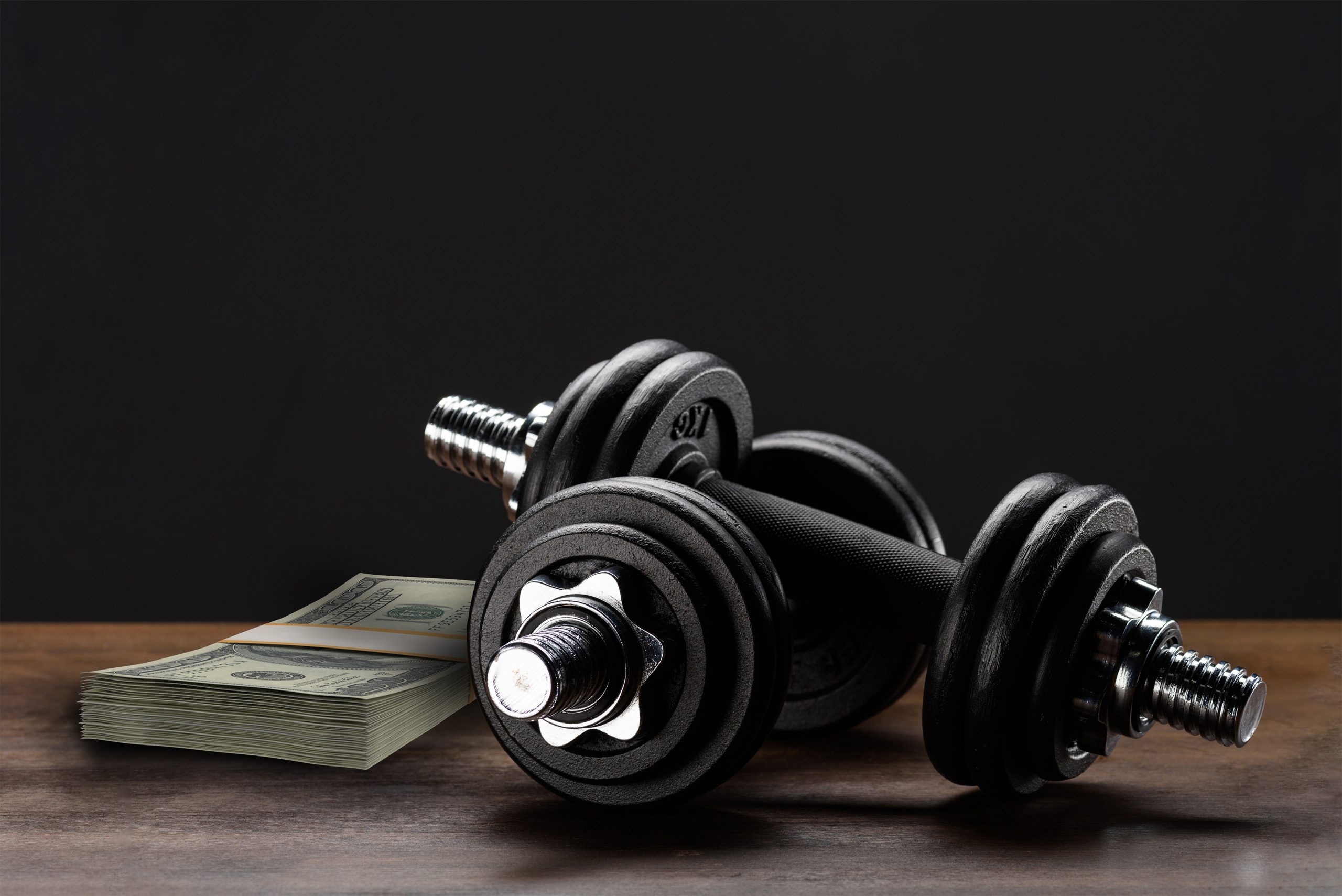 Bundles of $100 bills next to dumbells symbolizing monthly gym operating expenses
